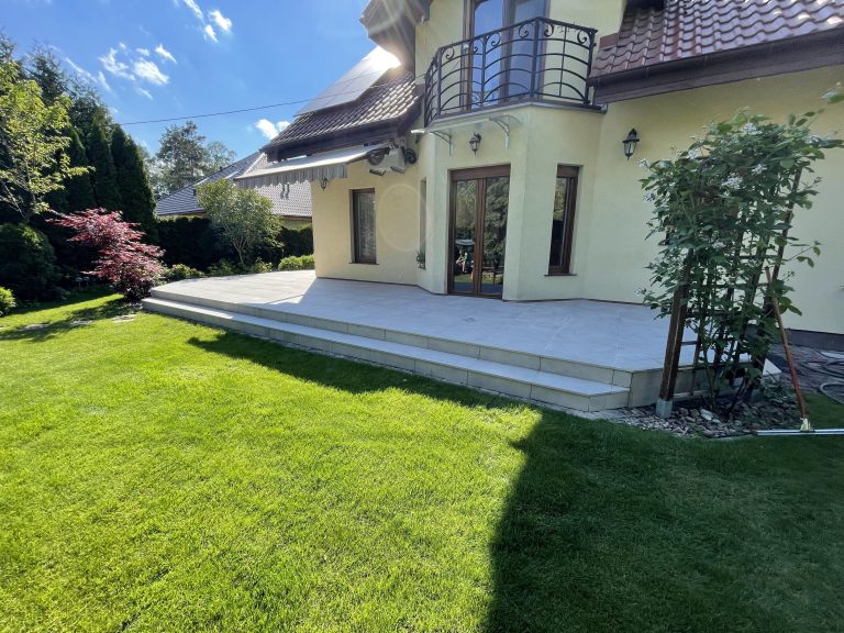 Taras zewnętrzny Poznań – przestronny jasny taras gresowy ze schodami przy eleganckiej willi z kutym balkonem i zadbanym ogrodem z trawnikiem